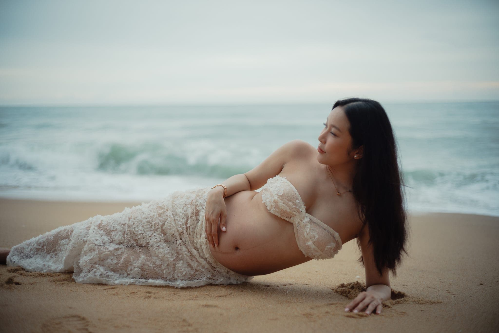 Lying along the sand, propped on an arm, the waves behind