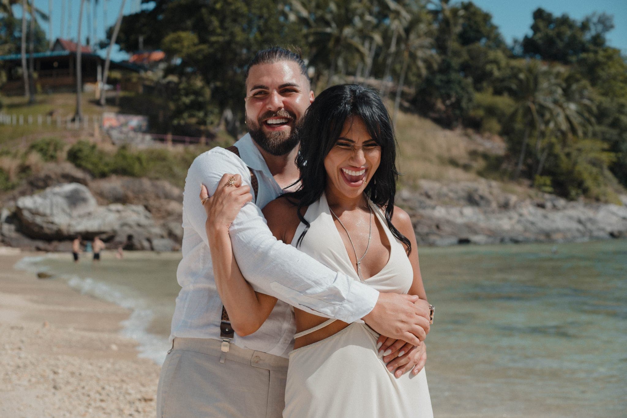 The bride and groom laughing in a hug with the bay behind them