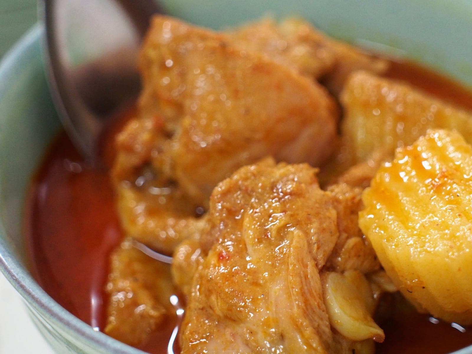 Chicken and potato matsaman curry in a pale green bowl, a spoon resting in the red sauce