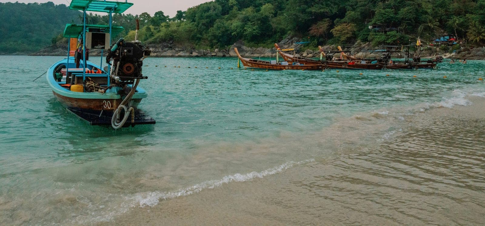 Longtail boats at the water's edge in a cove backed by jungle