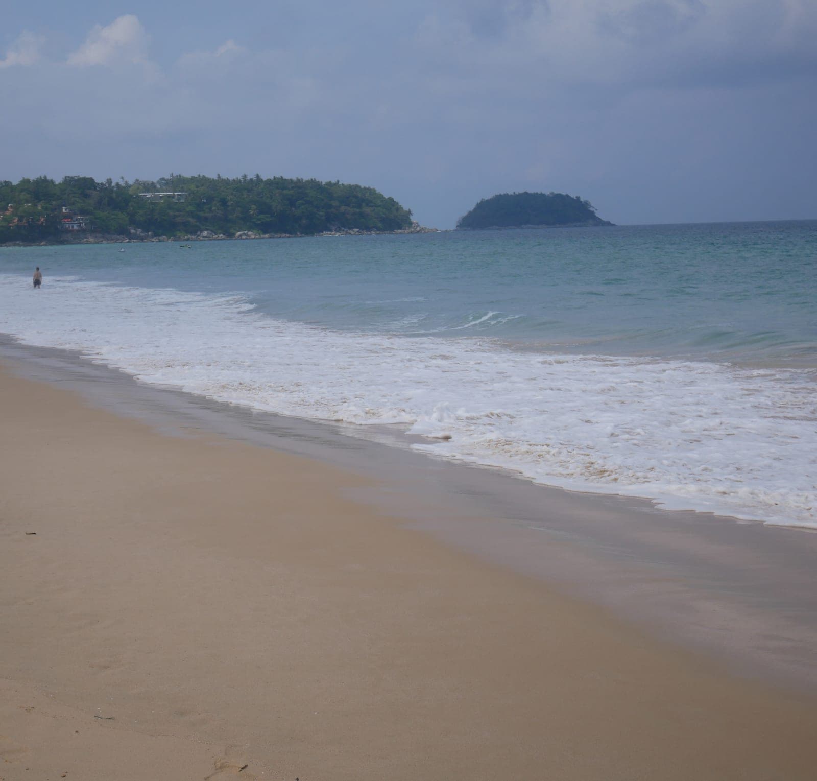 Karon's wide sand and surf under a grey sky, looking south to the headland and Ko Pu