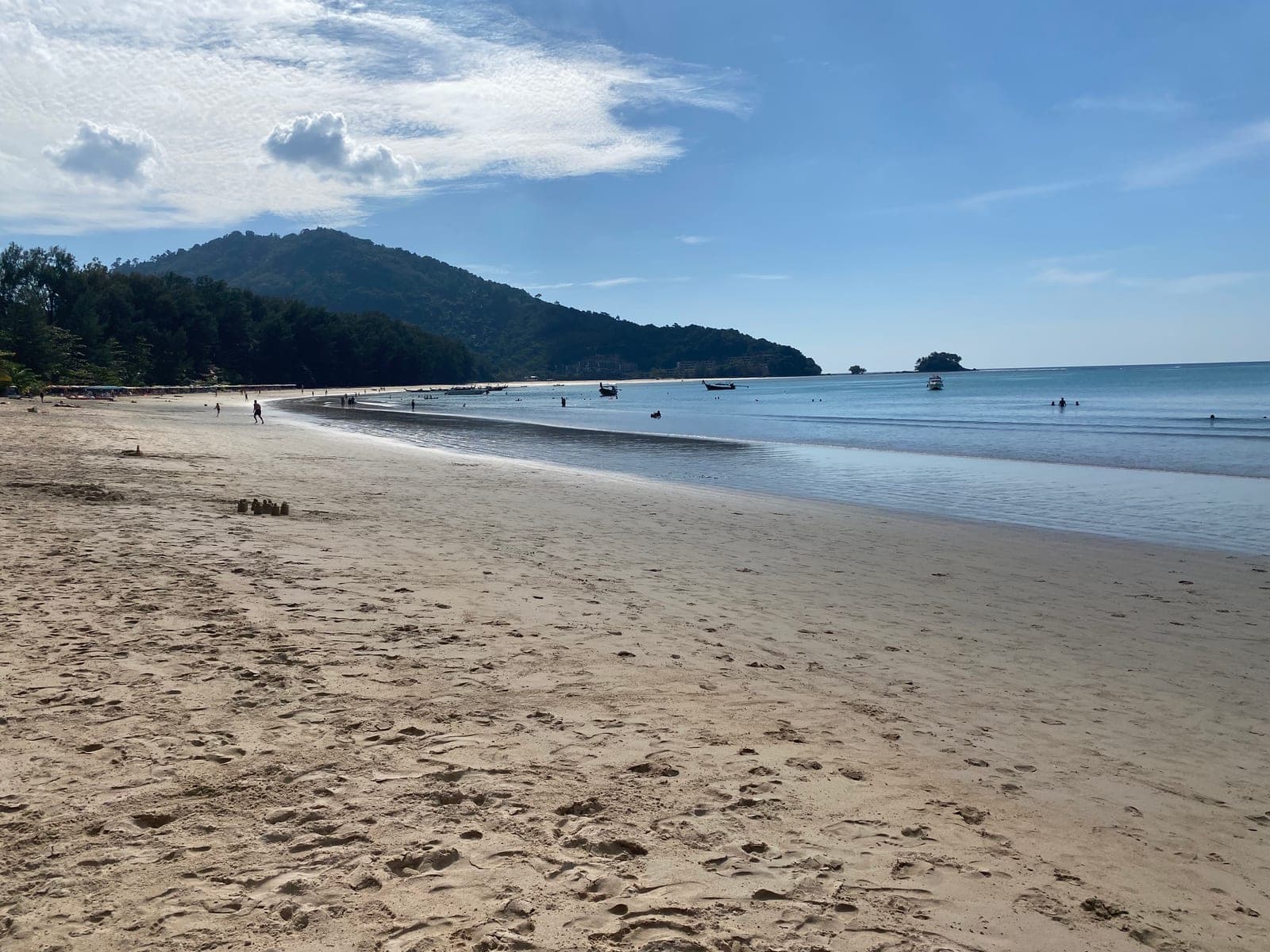Nai Yang's shallow bay at low tide, a row of umbrellas along the trees, longtail boats at anchor and a green headland behind