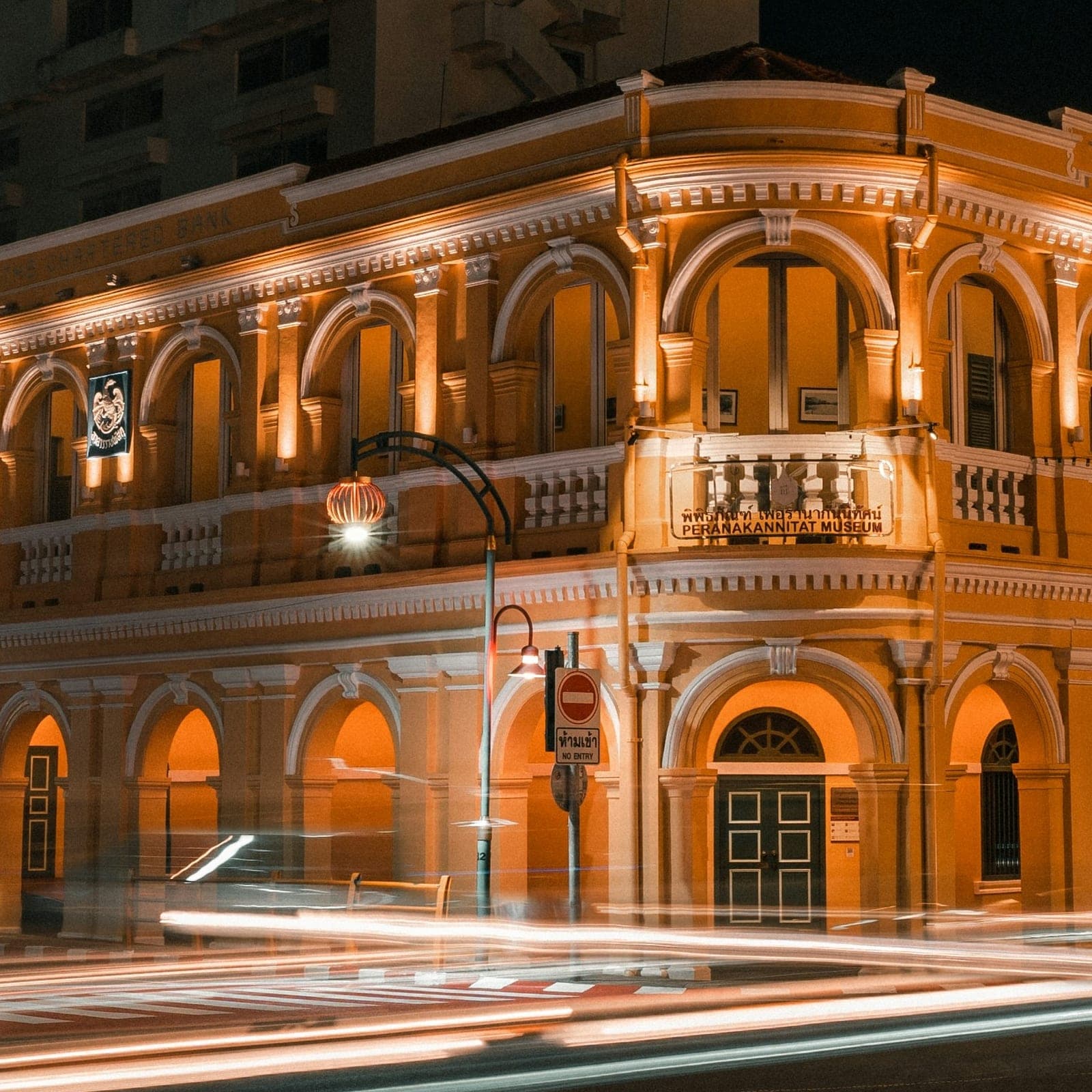 An arcaded two-storey corner building in Old Town lit gold at night, car lights streaking past across the empty junction