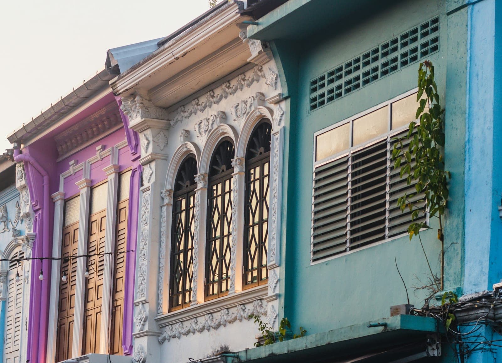 Shophouse fronts in violet, white, teal and blue, with carved stucco round tall shuttered windows