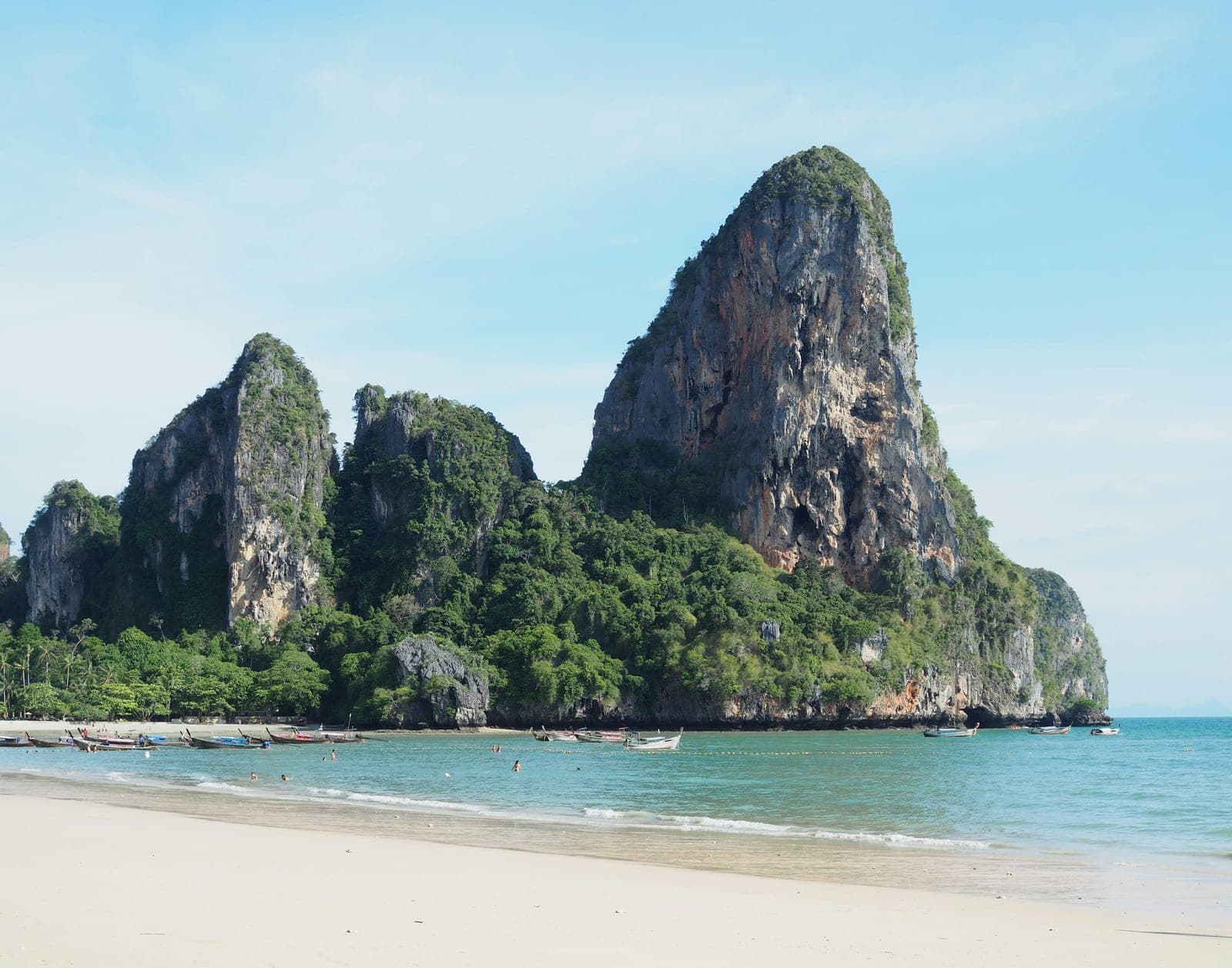 Limestone towers covered in forest rising over Railay's white beach, longtail boats moored in the turquoise bay