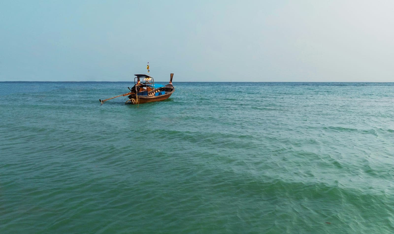An empty wooden longtail boat moored on calm green water off Rawai, a lifebuoy hanging under its canopy