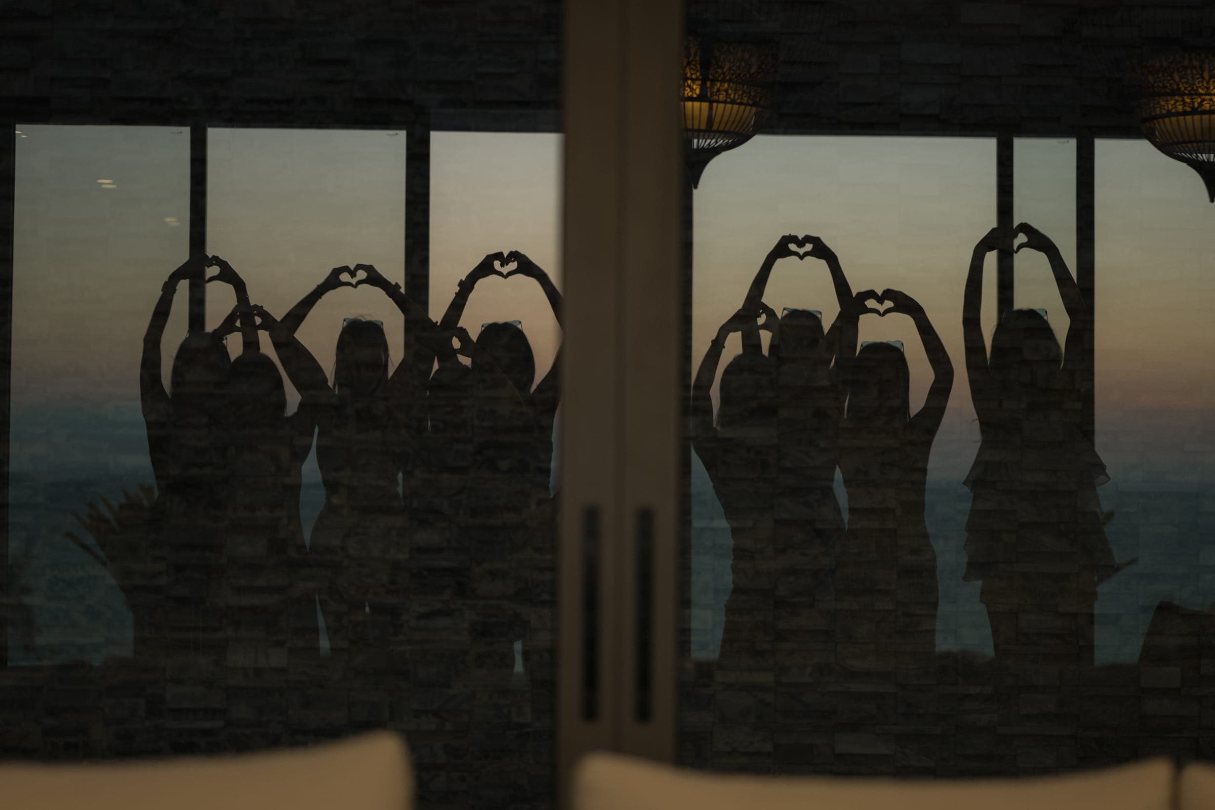 Friends silhouetted in a villa window at dusk, making heart shapes with their arms