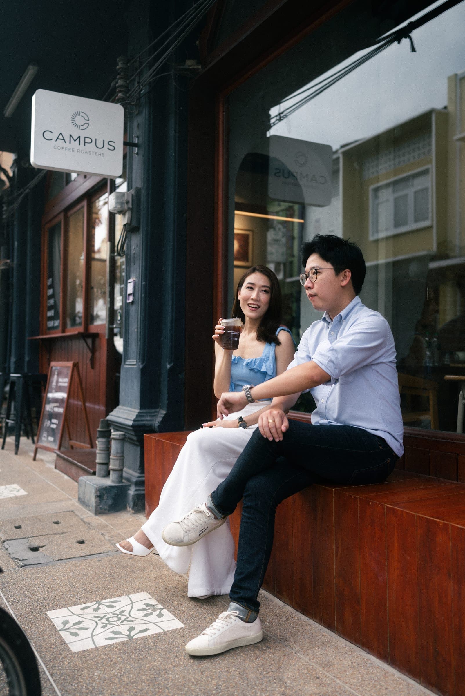 Couple sitting on a café bench in Old Town with an iced coffee, patterned tiles at their feet