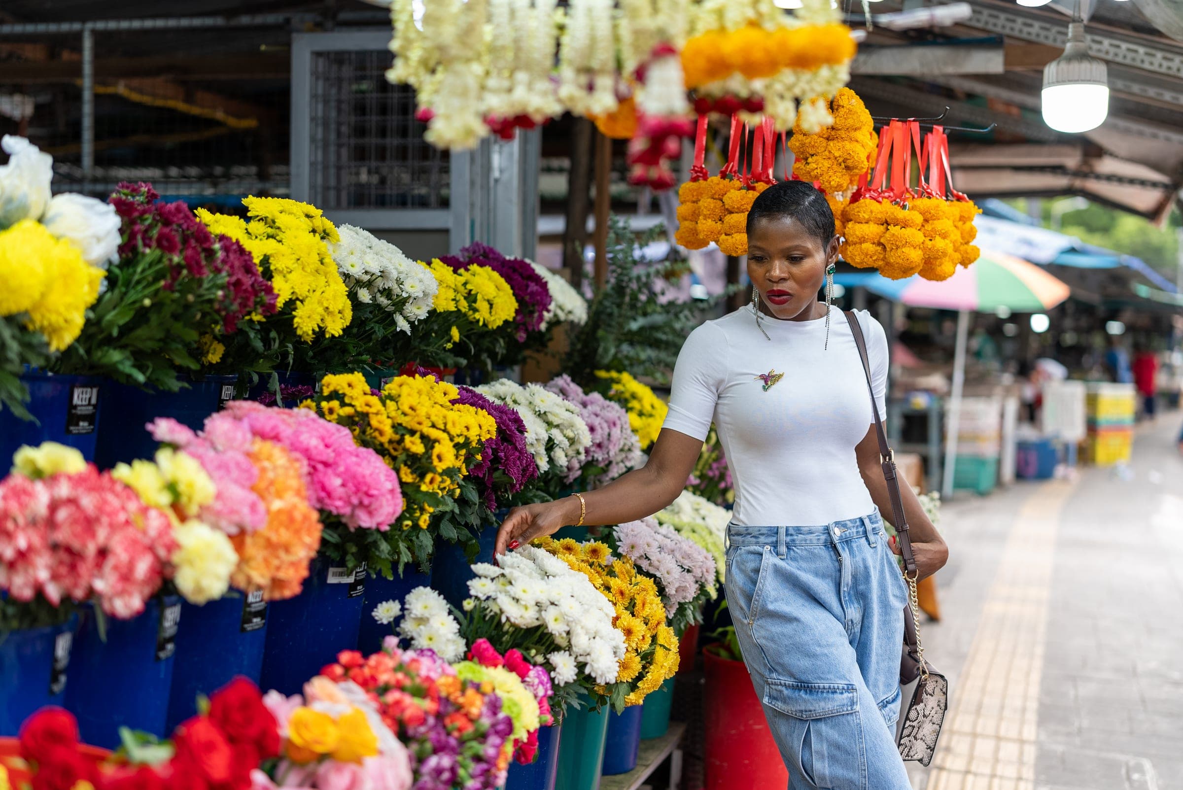 Woman walking past buckets of marigolds and roses at a flower market