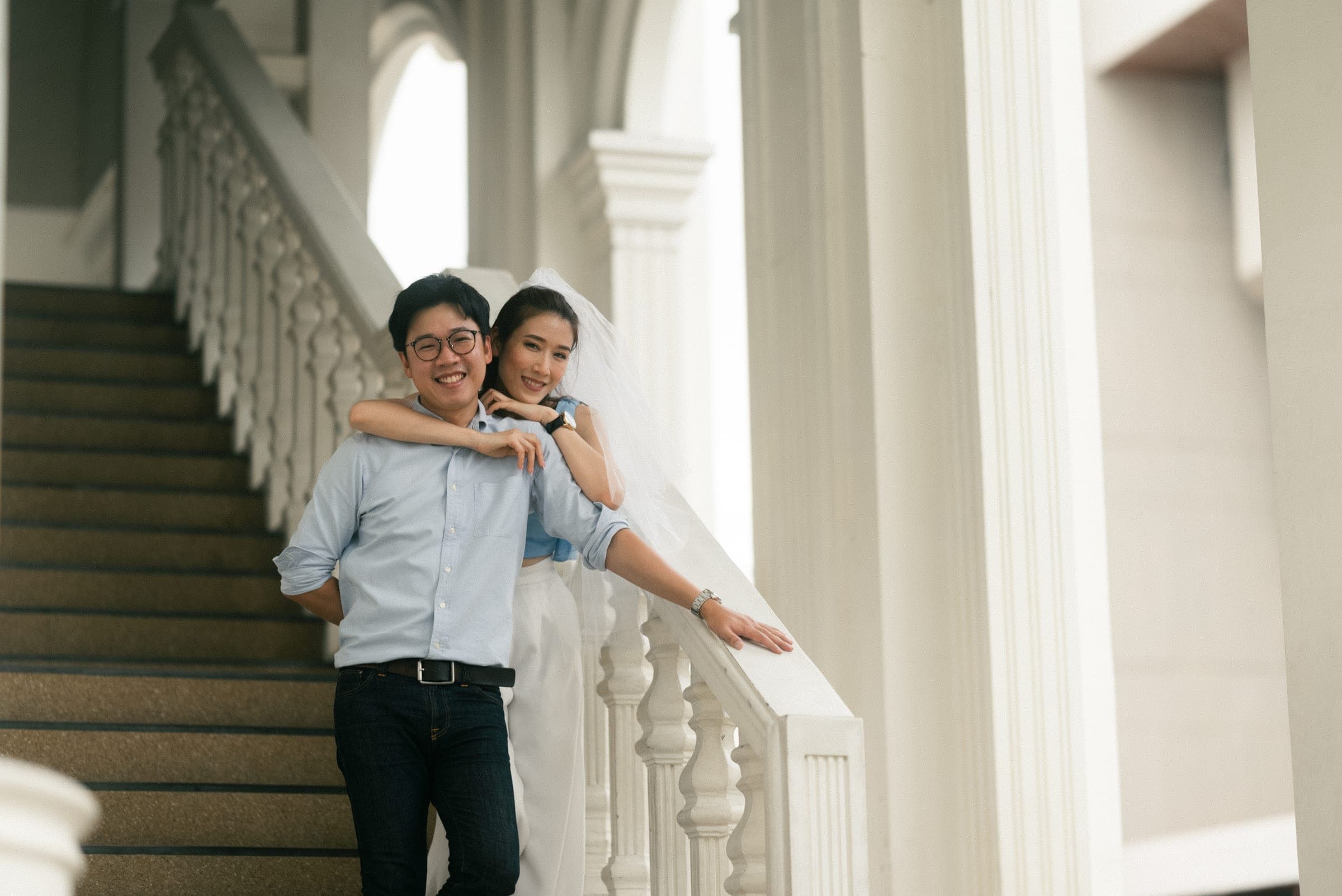 Couple on a white colonnaded staircase, one arm draped over the other’s shoulder