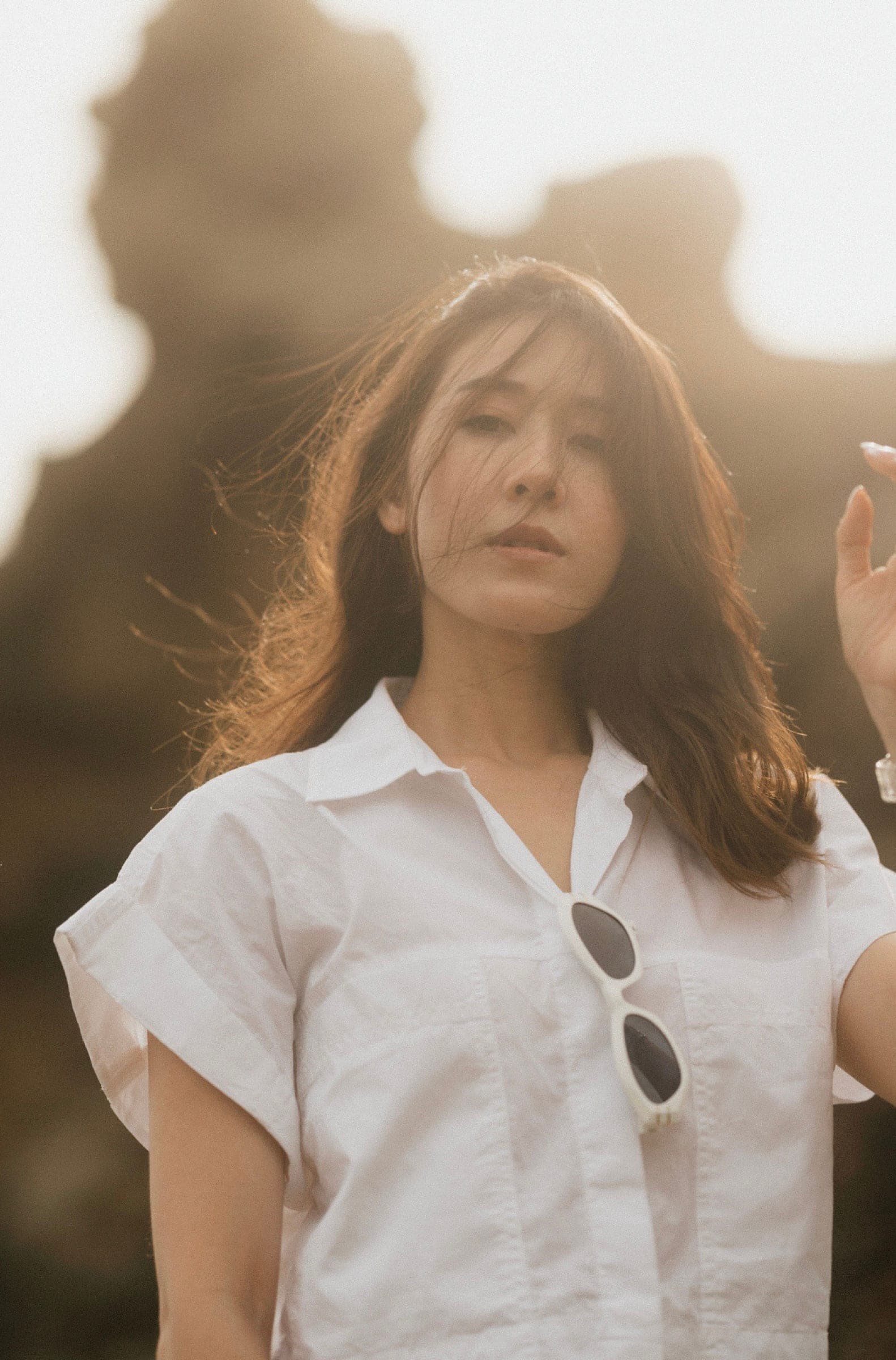 Backlit portrait of a woman in a white shirt, hair lifted by the wind, hazy rocks glowing behind her