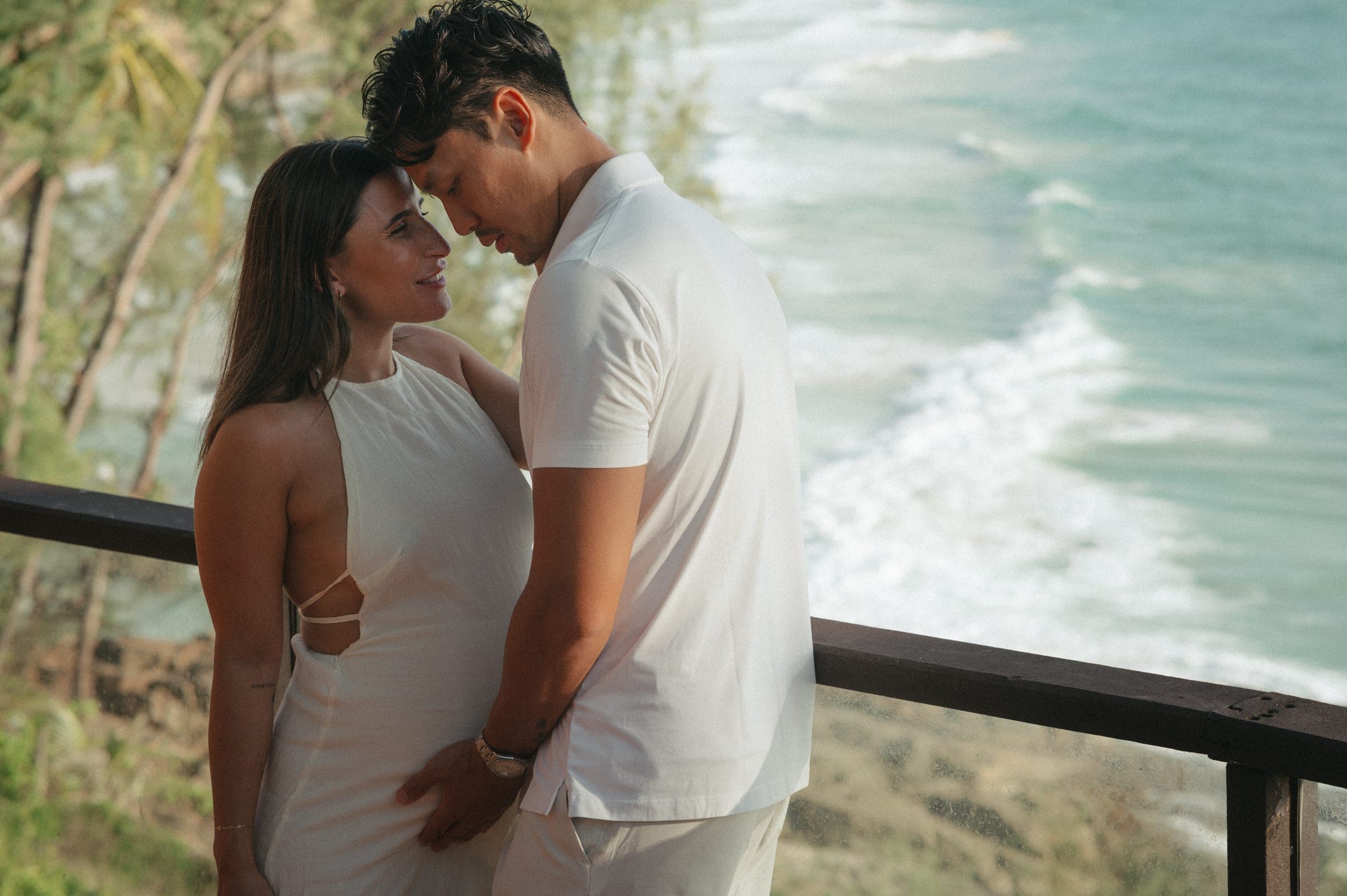 Couple in white on a balcony above the surf, foreheads touching