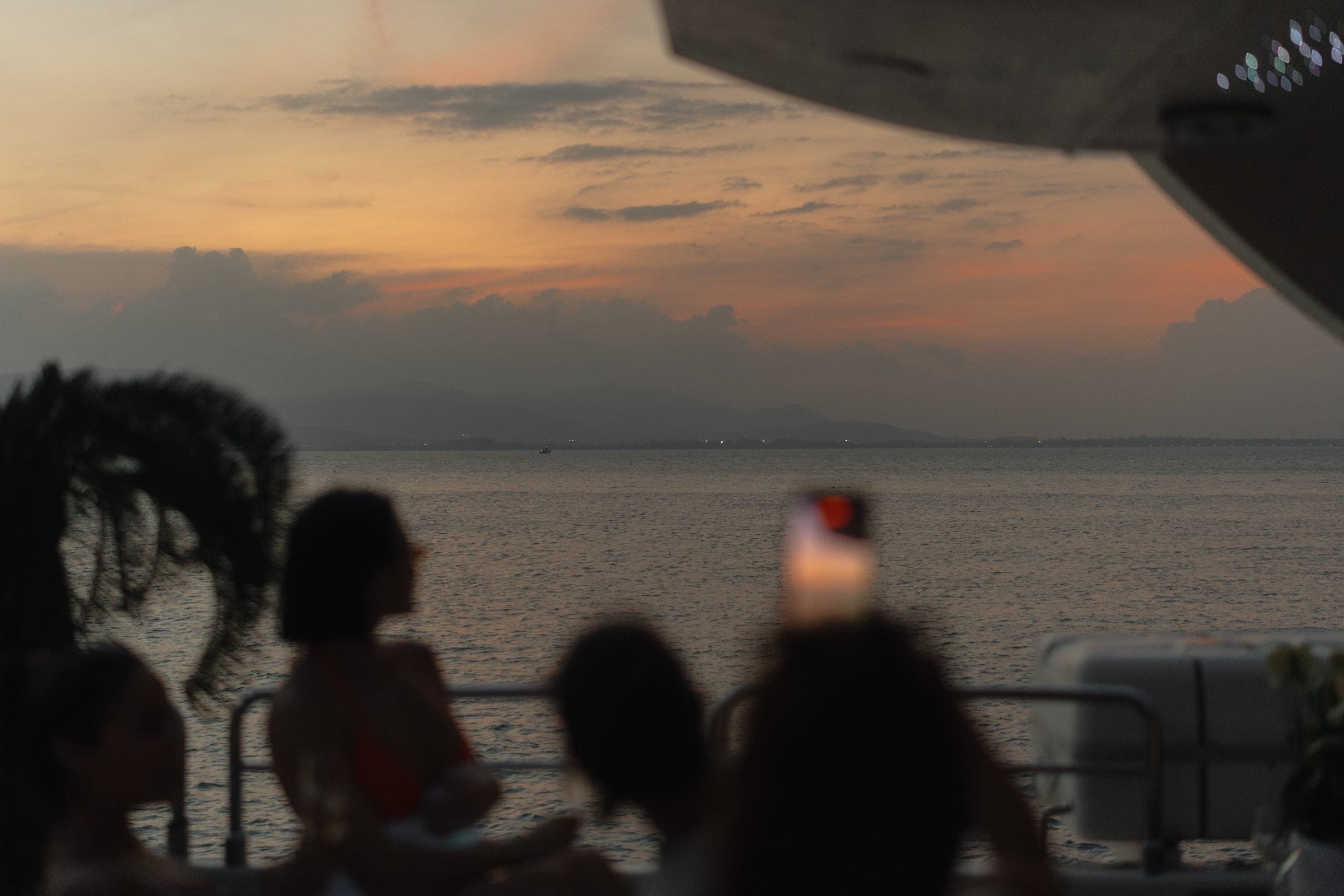 Sunset from the deck of a boat, silhouettes holding phones up to the orange sky