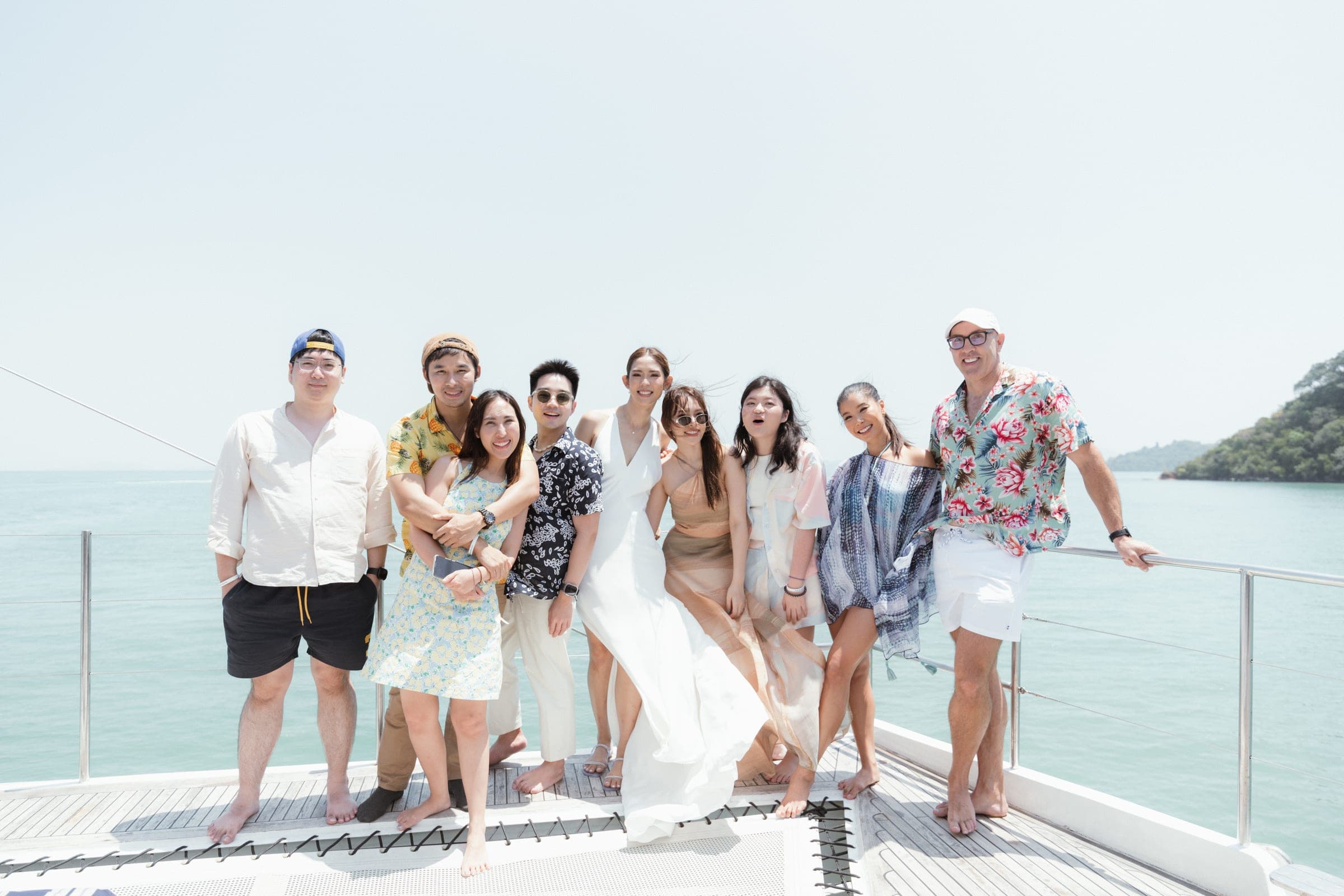 Friends in shirts and dresses lined up at the bow, sea and islands behind
