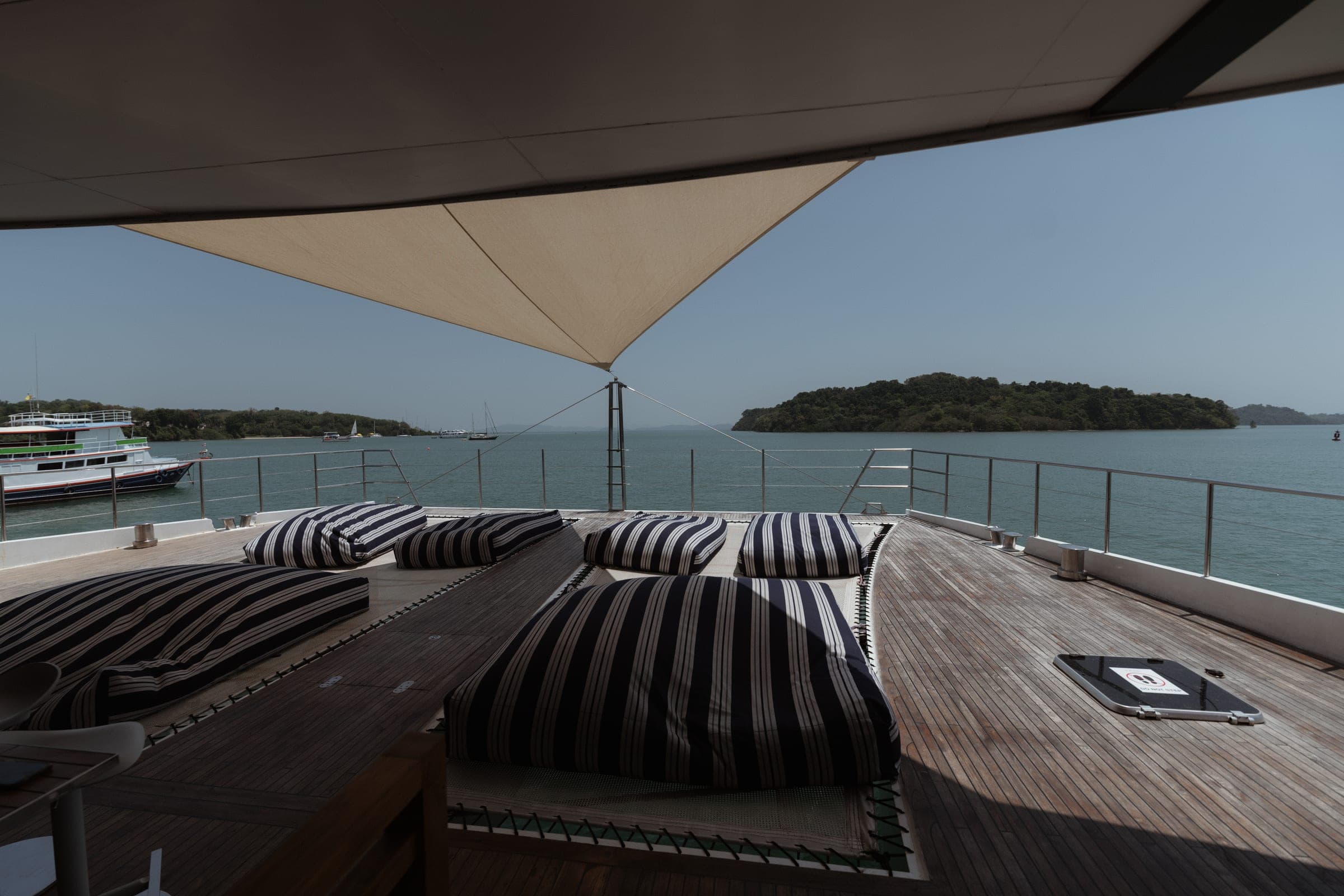 Empty striped cushions on a yacht deck under a shade sail, an island off the bow