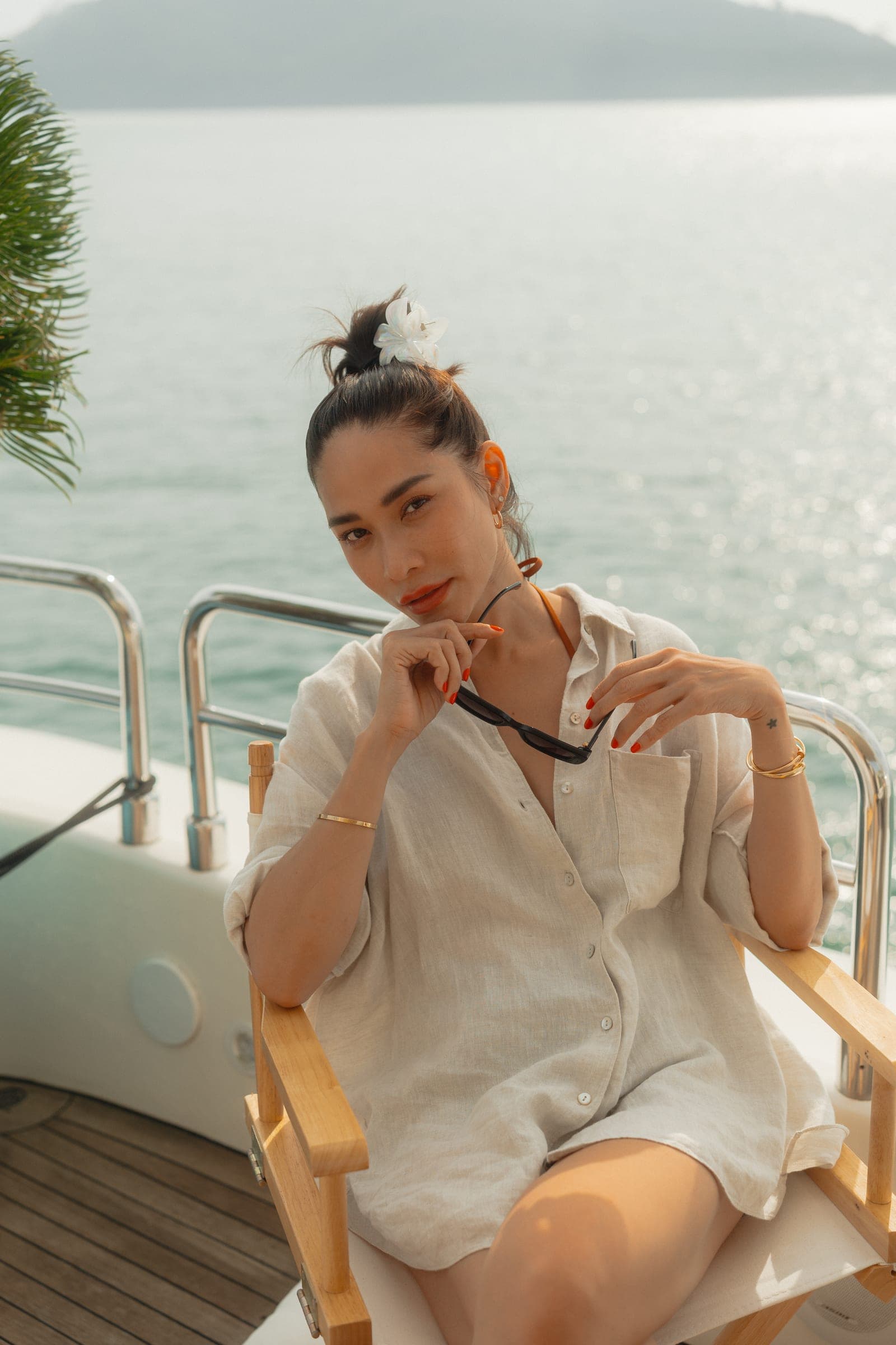 Woman in a linen shirt in a director’s chair on deck, the sea glittering behind