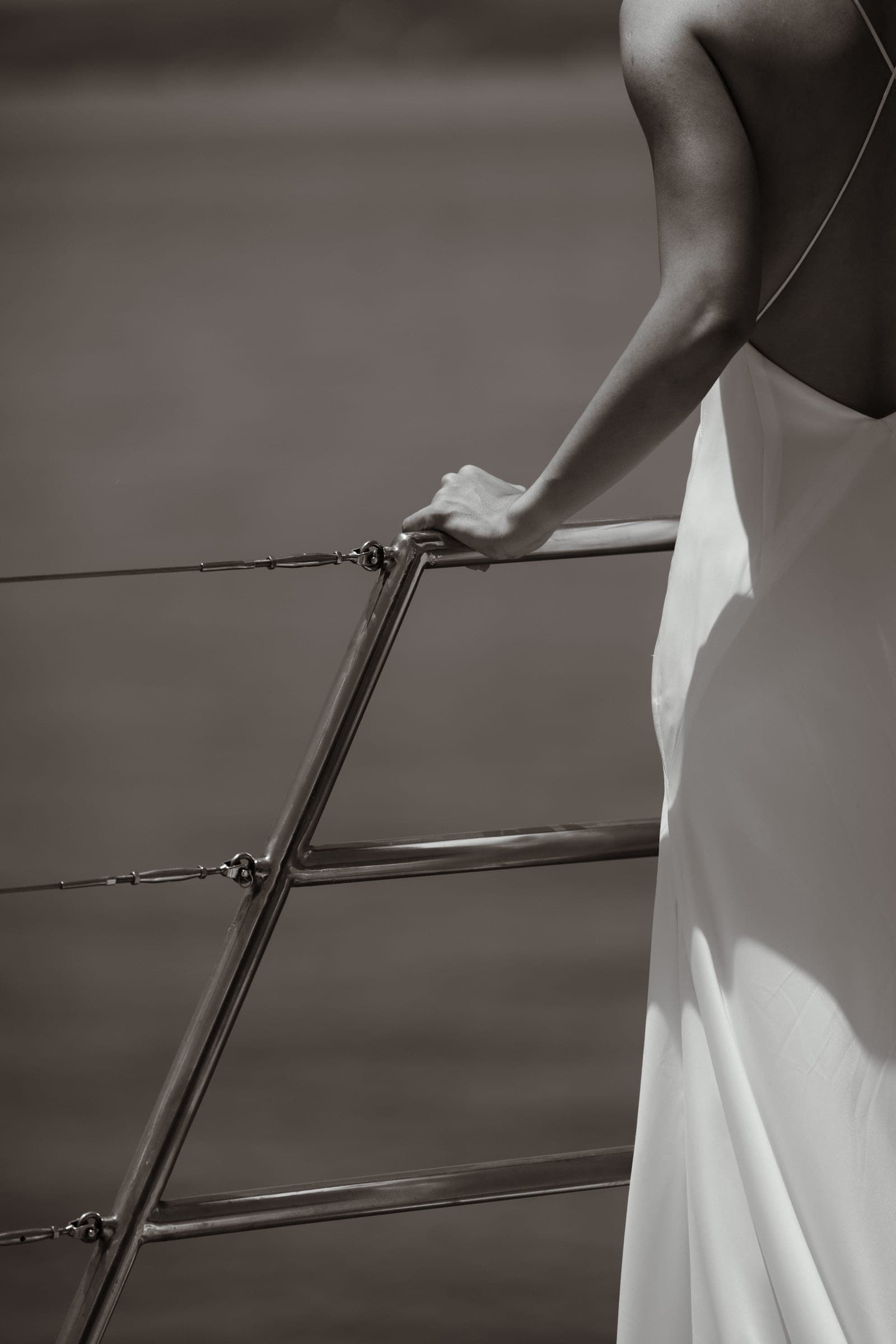Black-and-white detail of a hand on a yacht rail and the fall of a white dress